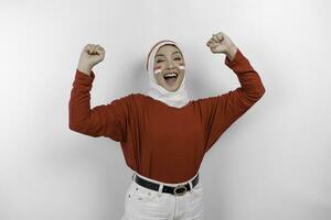 en ung asiatisk muslim kvinna med en Lycklig framgångsrik uttryck bär röd topp och vit hijab isolerat förbi vit bakgrund. Indonesiens oberoende dag begrepp. foto