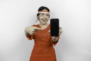 en porträtt av en leende asiatisk kvinna bär röd kebaya och pannband och som visar henne telefon, isolerat förbi vit bakgrund. Indonesiens oberoende dag begrepp foto