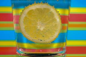 citronsaft brusande dryck i en klar glas med färgrik bakgrund som visar brusande bubblor foto