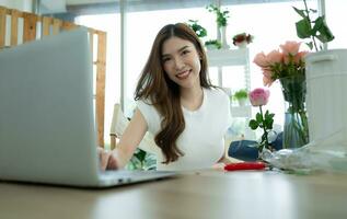 skön asiatisk kvinna arbetssätt med bärbar dator dator på blommig affär. foto