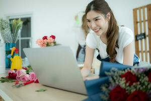 ung asiatisk kvinna blomsterhandlare arbetssätt med bärbar dator i blomma affär foto