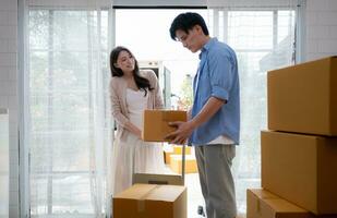 ung asiatisk par rör på sig i ny hus. asiatisk man och kvinna innehav lådor. foto