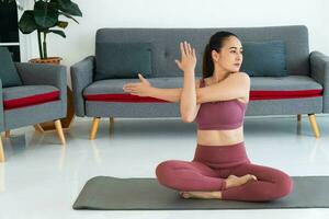 asiatisk ung friska kvinna i sportartiklar praktiserande yoga på Hem, sport flicka mediterar i levande rum på Hem foto