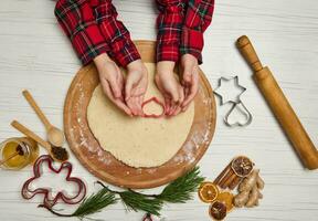 jul och ny år firande traditioner. traditionell festlig mat tillverkning, familj kulinariska. platt lägga av barn händer skärande småkakor av rå pepparkaka deg foto