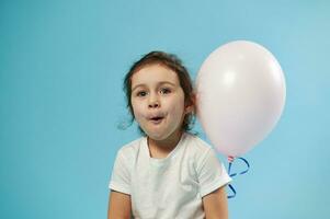 glad liten flicka ser på kamera medan Framställ med en ping luft ballong på blå bakgrund med kopia Plats foto