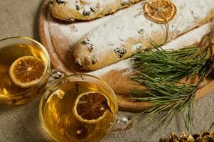 närbild av glas koppar med ört- te och skivor av torkades citrus- Nästa till en trä- styrelse med hemlagad utsökt nyligen bakad tysk traditionell stollen bröd stänkte med glasyr socker. jul. foto