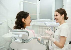 besök till tandläkare hygienist. bak- se av en kvinna i tandläkare stol under regelbunden dental utnämning i vit samtida tandvård klinik med modern Utrustning. oral vård och dental hygien begrepp foto