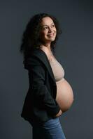 skön äkta gravid kvinna, innehav henne gravid mage, leende sött ser åt sidan, isolerat på studio bakgrund foto