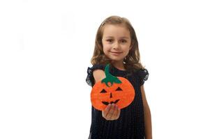 isolerat porträtt på vit bakgrund med kopia Plats av förtjusande liten flicka, 4 år gammal Söt unge, innehav en hemlagad filtskuren pumpa, symbol av de halloween fest, och som visar den till de kamera foto
