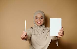 charmig arab muslim kvinna med skön leende innehav en vit dagbok och penna. foto