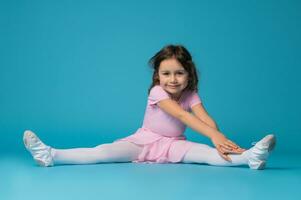 skön liten flicka ballerina Sammanträde på en blå bakgrund, praktiserande och stretching henne kropp foto