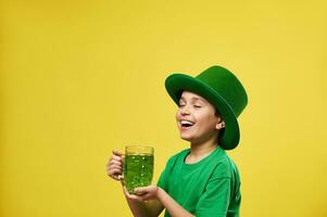 Lycklig pojke i pyssling hatt njuter grön dryck stående på yelow backgroud med kopia Plats . helgon Patricks dag foto