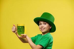 leende Lycklig caucasian pojke i irländsk grön hatt innehar en glas med grön dryck poser på kamera. helgon Patricks dag foto