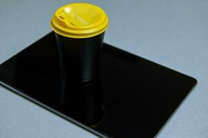 Artikel fotografera. kopia Plats. kaffe i svart papper glas med en gul lock på en svart läsplatta. topp se på en grå bakgrund foto