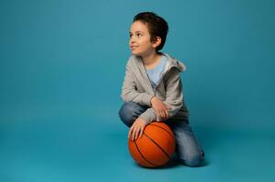 skön sportig Tonårs pojke Framställ med en boll för spelar basketboll över blå bakgrund foto