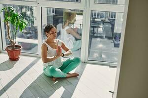 uppmärksam kvinna utför padmasana, andas in luft och håller på med andas övningar under yoga öva på Hem foto