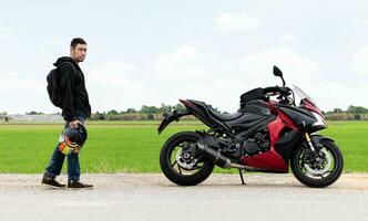 cyklist man hand håll hjälm och motorcykel med ris fält bakgrund foto