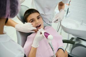 modig skola pojke i de tandläkarens stol under en dental kolla upp, tar emot tänder behandling på pediatrisk tandvård klinik. begrepp av tidigt diagnos av karies och i god tid behandling av dental sjukdomar foto