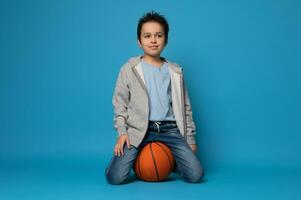 isolerat porträtt av en Tonårs basketboll spelare Sammanträde på ett orange boll foto