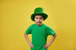 arg pojke bär pyssling grön hatt poser till de kamera på en gul bakgrund. helgon Patricks dag. kopia Plats foto