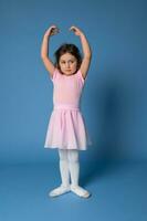 en graciös liten ballerina utför poser i balett dansa, stående isolerat över blå bakgrund foto