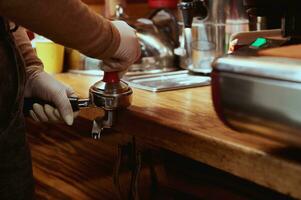 närbild av kvinna barista händer härdning, brådskande jord kaffe i metall portafilter. trampning kaffe foto