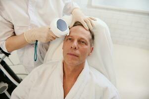 stilig mogna europeisk man mottar en ansiktsbehandling konturering procedur med meso trådar för ansikte föryngring, anti-åldring, ansiktslyftning, mesoterapi förfaranden på de wellness spa. manlig kosmetologi begrepp foto
