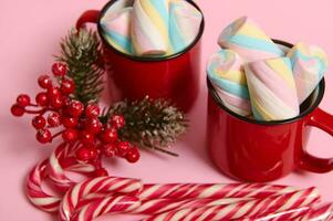 närbild, beskurna bild av jul föremål, randig sugary godis käppar, järnek och råna med varm dryck och våt färgrik marshmallows på rosa färgad bakgrund med kopia Plats för jul ad foto