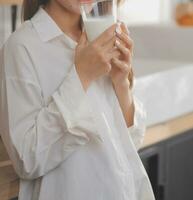 porträtt av en nöjd ung asiatisk kvinna dricka mjölk från de glas isolerat över vit bakgrund foto