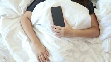 sömnlös kvinna kan inte sömn liggande i säng sent på natt påfrestande till sömn och hand innehav smartphone foto