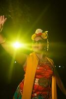 en skön Sundanesiska dansare poser och danser i en glamorös klänning och scarf i främre av de skede ljus foto