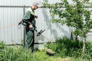 en man klipper gräsmatta gräs med en gräsmatta gräsklippare. bensin gräsmatta gräsklippare, trimmer närbild. man arbetssätt i de trädgård foto