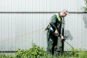 en man klipper gräsmatta gräs med en gräsmatta gräsklippare. bensin gräsmatta gräsklippare, trimmer närbild. man arbetssätt i de trädgård foto