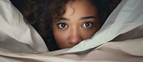 afrikansk flicka dölja ansikte under filt medan liggande i säng foto