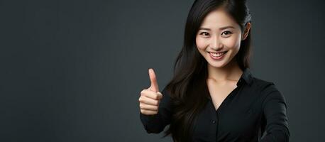 attraktiv asiatisk kvinna ger tummen upp på grå bakgrund tom område foto