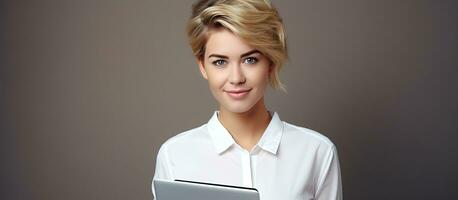 blond kvinna med kort hår innehav arbete bärbara datorer och en bärbar dator i en vit skjorta och jeans mot en tom Plats företag aning foto