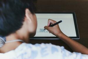 närbild ung skola pojke med nål penna skrivning på digital anteckningsblock. foto