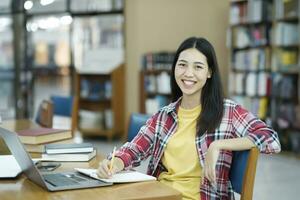 porträtt av en smart skön asiatisk flicka studing och läsning text böcker leende ser på kamera. foto