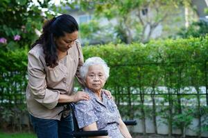 vårdgivare hjälpa asiatisk äldre kvinna funktionshinder patient sitter på rullstol i parken, medicinsk koncept. foto