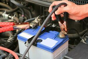 bil mekaniker användningar batteri hoppare kablar avgift en död- batteri. foto