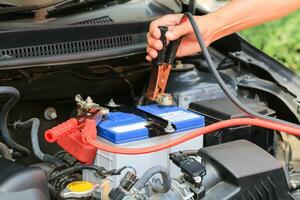 bil mekaniker användningar batteri hoppare kablar avgift en död- batteri. foto