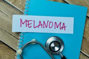 begrepp av melanom skriva på klibbig anteckningar med stetoskop isolerat på trä- tabell. foto