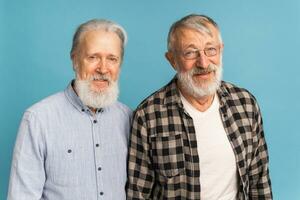 porträtt två äldre man vänner stående över blå bakgrund - vänskap, åldrig och senior människor foto