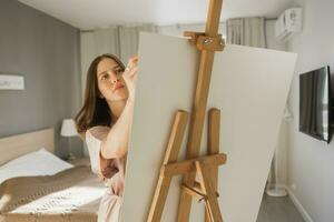 ung kvinna konstnär målning på duk på de staffli på Hem i sovrum - konst och kreativitet begrepp foto