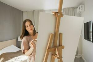 ung kvinna konstnär målning på duk på de staffli på Hem i sovrum - konst och kreativitet begrepp foto