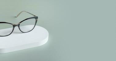 podium med glasögon på pastell grön bakgrund. optisk Lagra, syn testa, eleganta glasögon begrepp. foto