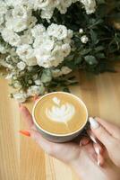 kaffe latte med kvinna hand och blommor på Kafé tabell foto