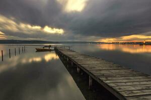 de lång exponering se på en molnig dag på de sjö med en båt på en trä- pir. foto