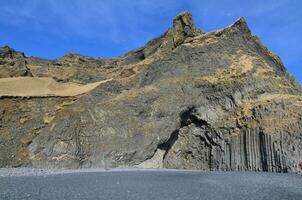 basalt sten formationer på svart sand strand i island foto