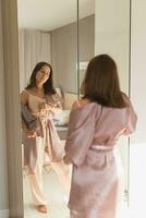 Lycklig morgon. attraktiv ung kvinna ser i spegel på henne lägenhet - vakna upp och ny dag foto